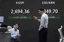 Currency traders work near a screen showing the Korea Composite Stock Price Index…